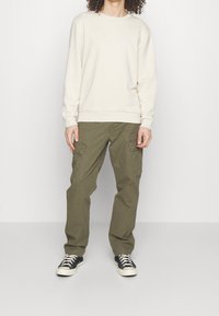 Lichtbeige katoenen sweatshirt met een ronde hals, gecombineerd met olijfgroene cargo broek met zijzakken en zwarte sneakers.