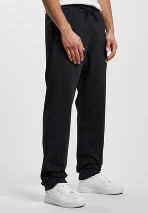 Schwarze Jogginghose mit einem Kordelzugbund, Seitentaschen und einer lockeren Passform, kombiniert mit weißen Turnschuhen. Glatte Stoffoberfläche.