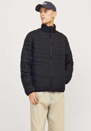 Black puffer jacket with ribbed design, high collar, and front zipper. Worn over light-colored jeans, minimalistic style, textured fabric.