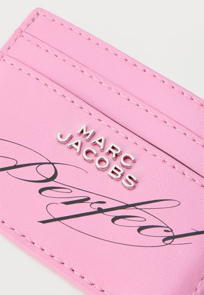 Ροζ δερμάτινη θήκη κάρτας με ραμμένες άκρες, ανάγλυφο ασημί λογότυπο "Marc Jacobs" και μαύρο κείμενο με καλλιγραφικά γράμματα εν μέρει ορατό.