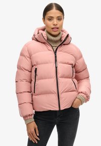 Giacca puffa rosa con cappuccio, chiusura a zip e due tasche laterali. Presenta polsini a coste e una texture liscia e lucida.
