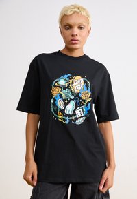 Black oversized t-shirt featuring a colorful graphic design with roses, dice, and various symbols. Made of soft cotton material.
