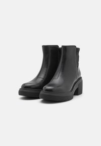 Botas de tobillo de cuero negro con cierre de cremallera, suela de goma gruesa, punta redondeada y tacón texturizado. Superficie lisa sin patrones visibles.