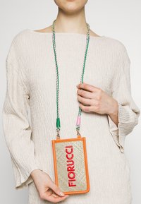 Orange- og guldfarvet rektangulær telefon-crossbodytaske med fletbånd i grøn, pink og lilla; har "FIORUCCI" i rødt. Tekstureret finish.