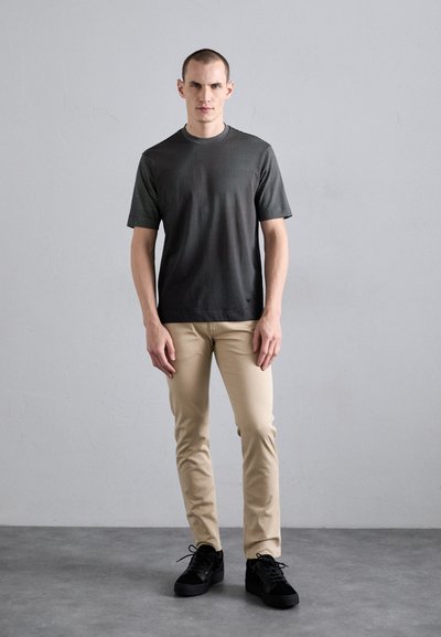 Short-sleeve black and gray patterned T-shirt with a crew neckline, paired with beige slim-fit pants and black sneakers.