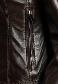 Temno rjava usnjena jakna iz bližine, ki prikazuje zadrgo s kovinsko zaponko in podrobno šivano.