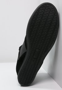 Semelle de sneaker noire avec un motif de semelle ondulée, fabriquée en caoutchouc et en daim, mettant en valeur un contraste de textures et un détail de logo subtil.