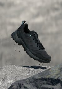 Black hiking shoe with a textured mesh upper, rubber sole, and light blue accents. Features signature stripes and a pull tab on the heel.