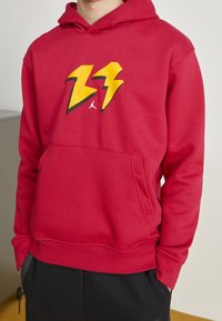 Sudadera con capucha roja y bolsillo delantero, con un diseño de rayo en colores amarillo y negro. Material de algodón, corte relajado.