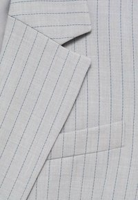 Tissu gris clair avec de fines rayures verticales foncées montrant le revers et la poche d'une veste de costume.
