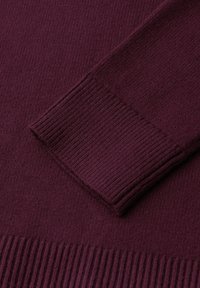 Närbild av en mörklila stickad tröja med ärm som visar ribbad manschett och texturerad tygkropp.