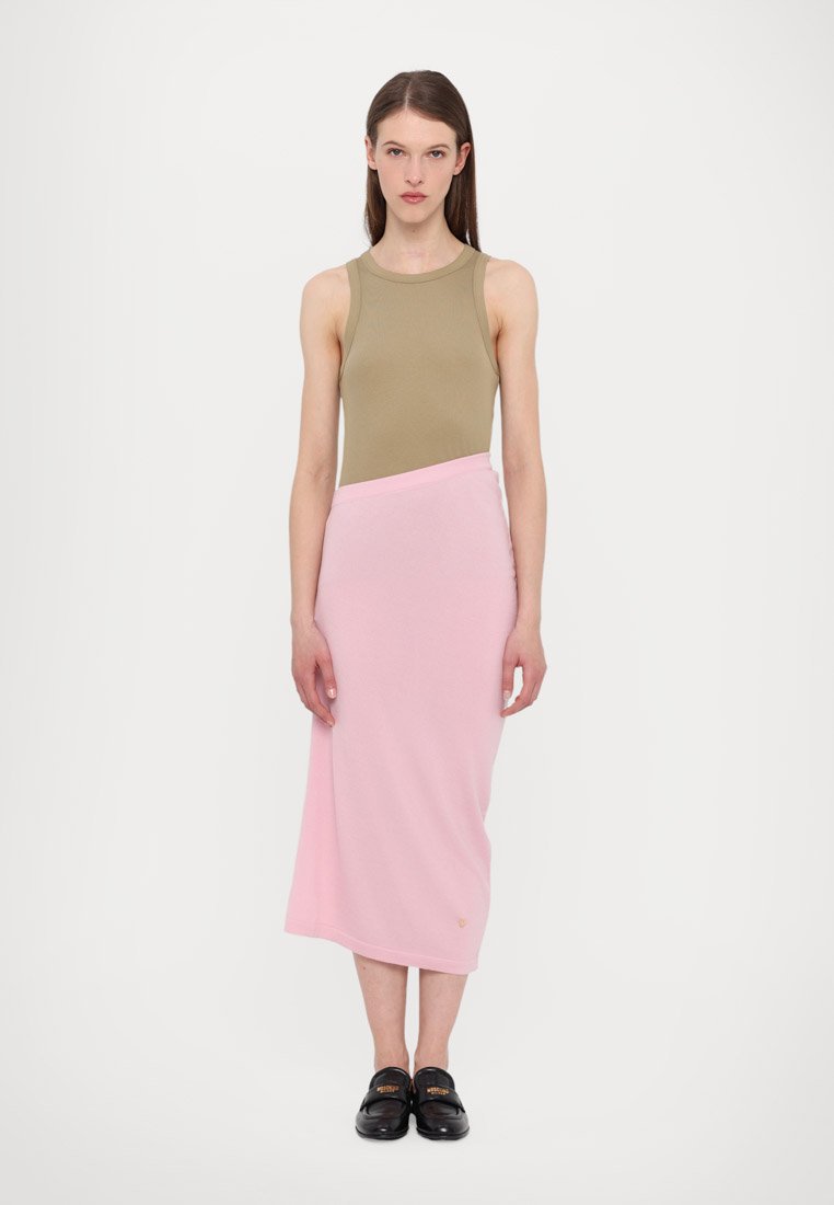 Débardeur vert olive associé à une longue jupe enroulée rose. Le tissu semble doux avec des coutures minimales. Des chaussures noires complètent la tenue.
