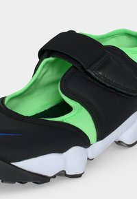 Μαύρο και πράσινο sneaker slip-on με λευκή τμηματοποιημένη σόλα και ρυθμιζόμενο μαύρο λουράκι στην κορυφή.