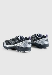 Scarpe da ginnastica nere e argento con tomaia in rete imbottita, sovrapposizioni testurizzate e una suola in gomma spessa. Accenti viola sul tallone.