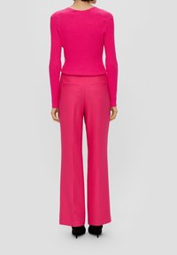 Aansluitende geribbelde roze trui met lange mouwen, gecombineerd met wijde roze broeken met achterzakken en gestyled met zwarte hakken.