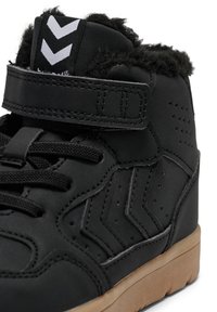 Sorte højhælede sneakers med en fuzzy krave, der har en velcro-strop, snørebånd og perforerede detaljer, placeret på en gummi gummisål.
