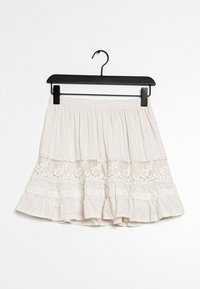 Jupe beige clair en tissu avec un design à volants. Fait de détails floraux brodés et d'une bordure en dentelle le long des couches. Taille élastique.