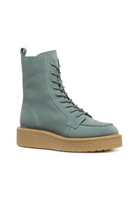 Stivale alla caviglia con lacci in morbida suede azzurro chiaro, con punta arrotondata e suola piatta beige spessa e testurizzata. Presenta un tassello sul retro per il sollevamento.