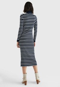 Navy ja valge triibuline ribakudum dress, millel on kõrge kaelus, pikad varrukad ja põlviniulatuv lõige, koos beežide pahkluu saabastega.