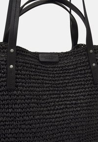 Zwarte geweven tote bag met leren handvatten. Bevat een textuur met een gevlochten ontwerp en een gegraveerd merklabel van zwart leer. Accenten van zilverkleurig beslag.