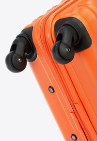 Valigia rigida arancione con doppie ruote nere, superficie texture e chiusura con zip. Include dettagli neri sugli angoli.
