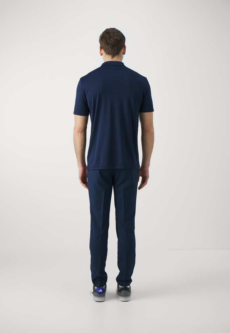 Polo à manches courtes bleu marine associé à un pantalon bleu marine, présentant une texture lisse, une coupe décontractée et une marque discrète sur les chaussures.