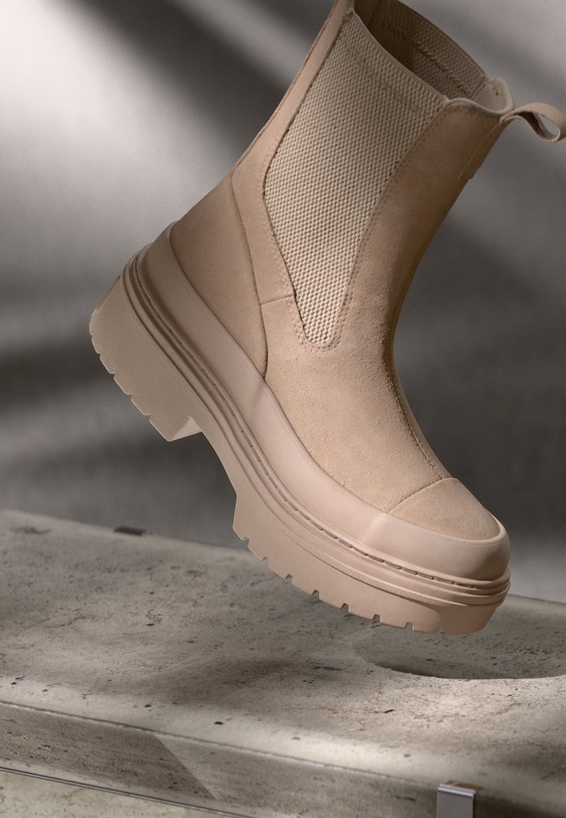 Botín beige con un panel de malla texturizado, suela gruesa y puntera reforzada. Diseño ligeramente estructurado con detalles de costura mínimos.