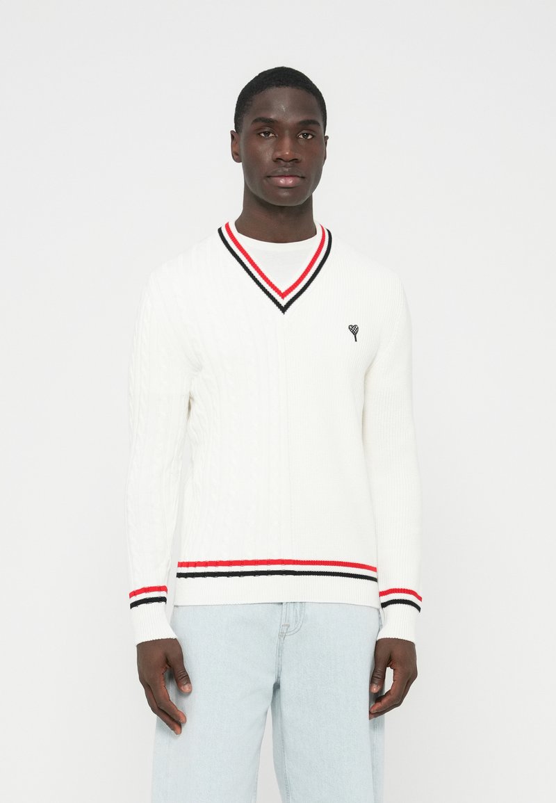 Baltas megztas megztinis su V formos iškirpte, apykaklėje ir apačioje raudonos bei juodos spalvų juostos. Ant krūtinės mažas juodas širdies logotipas.