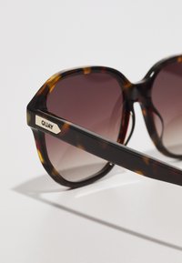 Tortoiseshell zonnebril in een grote achtkante vorm. Gradiënt donkere lenzen. Metalen accent met "QUAY" logo aan de zijkant. Soepele kunststof textuur.