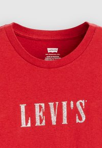 Rød bomull t-skjorte med rund hals og korte ermer, med "LEVI'S" i sølv rhinestone på forsiden. Pleielapp inkludert.