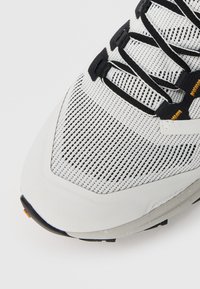 Weißer und schwarzer Netz-Laufschuh mit schwarzer Schnürung und orangefarbenen Nähdetails auf einem weißen Hintergrund.