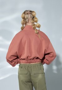 Felpa oversize color pesco con colletto alto e vita elasticizzata, abbinata a pantaloni cargo verde salvia con tasche posteriori.