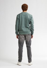 Felpa verde melangiata con maniche lunghe, colletto a giro e polsini in maglia. Abbinata a jeans di denim grigi e sneakers bianche.