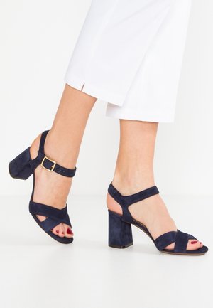 Granatowe sandały na wysokim obcasie zamszowe, z odkrytym palcem, z krzyżującymi się paskami i klamrą przy kostce. Obcas typu blok.
