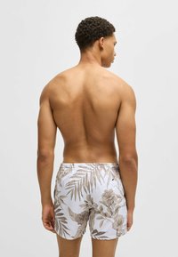 Herren-Badeshorts in Weiß mit braunen floralen und Palmenblättern. Sie verfügen über einen elastischen Taillenbund und einem leichten Stoff für Komfort.