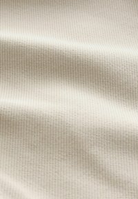Tela de crema texturizada con un patrón acanalado, que presenta sutiles variaciones en el tono y una superficie suave y lisa. Ideal para ropa liviana.