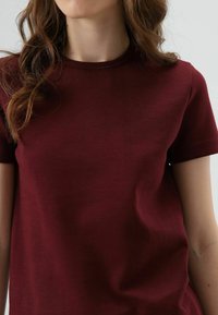 Bordeauxrode katoenen T-shirt met een ronde hals, korte mouwen en een gladde textuur. Minimalistisch ontwerp zonder zichtbare patronen of accenten.