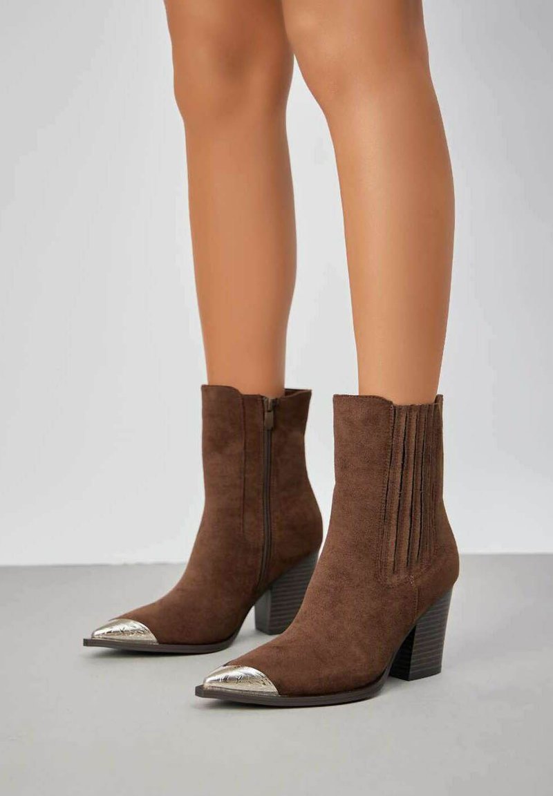 Bottes chevilles en daim marron avec un bout effilé et un embout argent métallique, dotées d'une fermeture éclair latérale et de détails de couture verticale, sur un talon empilé.