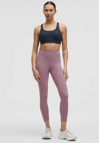 Sujetador deportivo negro, leggings rosa claro de cintura alta, textura suave, diseño ajustado. Zapatos deportivos blancos con detalles de malla y cordones.