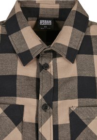 Brown and black plaid shirt with a button-up design, pointed collar, and two chest pockets. Made of cotton with a soft texture.