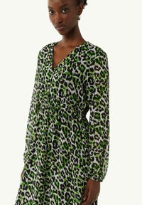 Leopardenmuster-Kleid in Grün und Schwarz, leichtes Material, lange Ärmel, V-Ausschnitt, taillierte Details, schwingt bis unter die Knie.