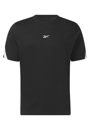 Camiseta de algodón negra con detalles blancos y logotipo, combinada con joggers blancos y zapatillas blancas. Cadena de oro al cuello.