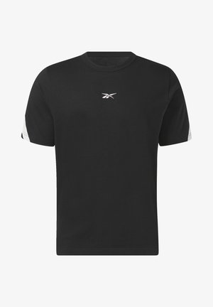 T-shirt en coton noir avec des accents blancs et un logo, associé à un jogging blanc et des baskets blanches. Chaîne en or autour du cou.