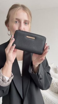 Black leather wallet with a textured finish, featuring a gold-tone logo plate. The zipper closure runs along the top edge.