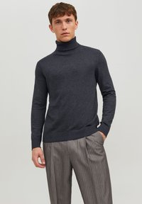 Pull à col roulé gris foncé au design ajusté, avec un col côtelé et des poignets, fabriqué en matériau tricoté doux, associé à un pantalon rayé gris clair.