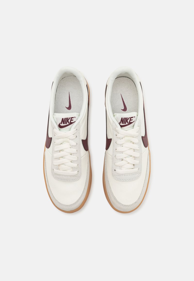 Sneakers Nike bianchi con swoosh maroon e suole in gomma, visti dall'alto, allacciati e posizionati affiancati su uno sfondo bianco.
