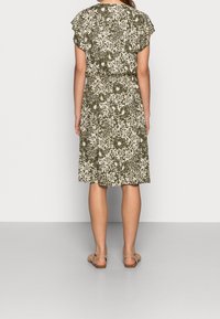 Olivově zelené květinové šaty s volným střihem, krátkými rukávy a stahovaným pasem. Obsahují bílé botanické vzory a délku ke kolenům.