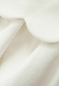 Bílá tkanina s texturovaným povrchem a zaobleným okrajem. Materiál působí měkce a lehce.