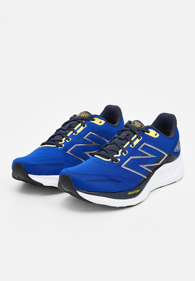 Zapatillas deportivas sintéticas azules con parte superior de malla, entresuela blanca y suela negra. Presenta acentos en amarillo y gris con cordones para un cierre seguro.