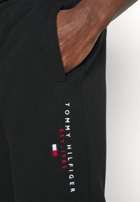 Sorte joggingbukser lavet af blødt stof, med sidelomme og broderet "TOMMY HILFIGER EST. 1985" med trefarvet flagdetaljer.